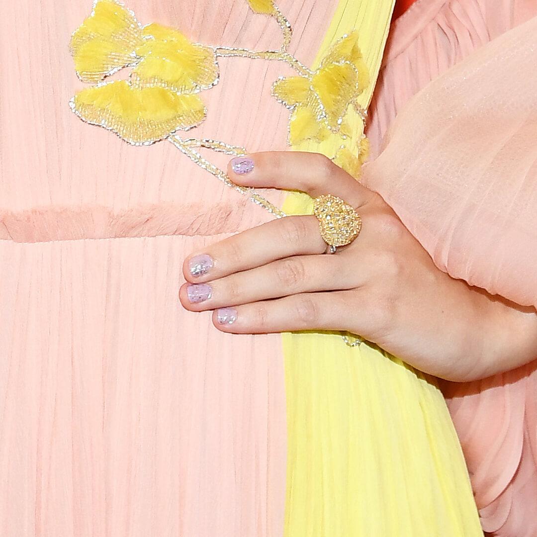 Close-up of Taylor Swift's glittery lavender nail art against her peach and yellow dress