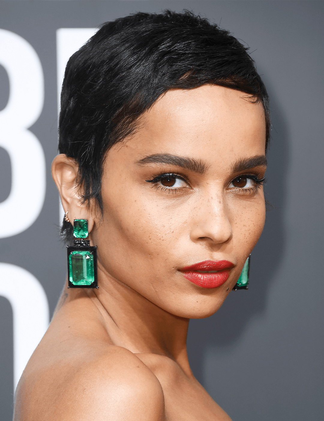Zoe Kravitz rocking a short pixie cut hairstyle, dangling emerald earrings, and red lips makeup look