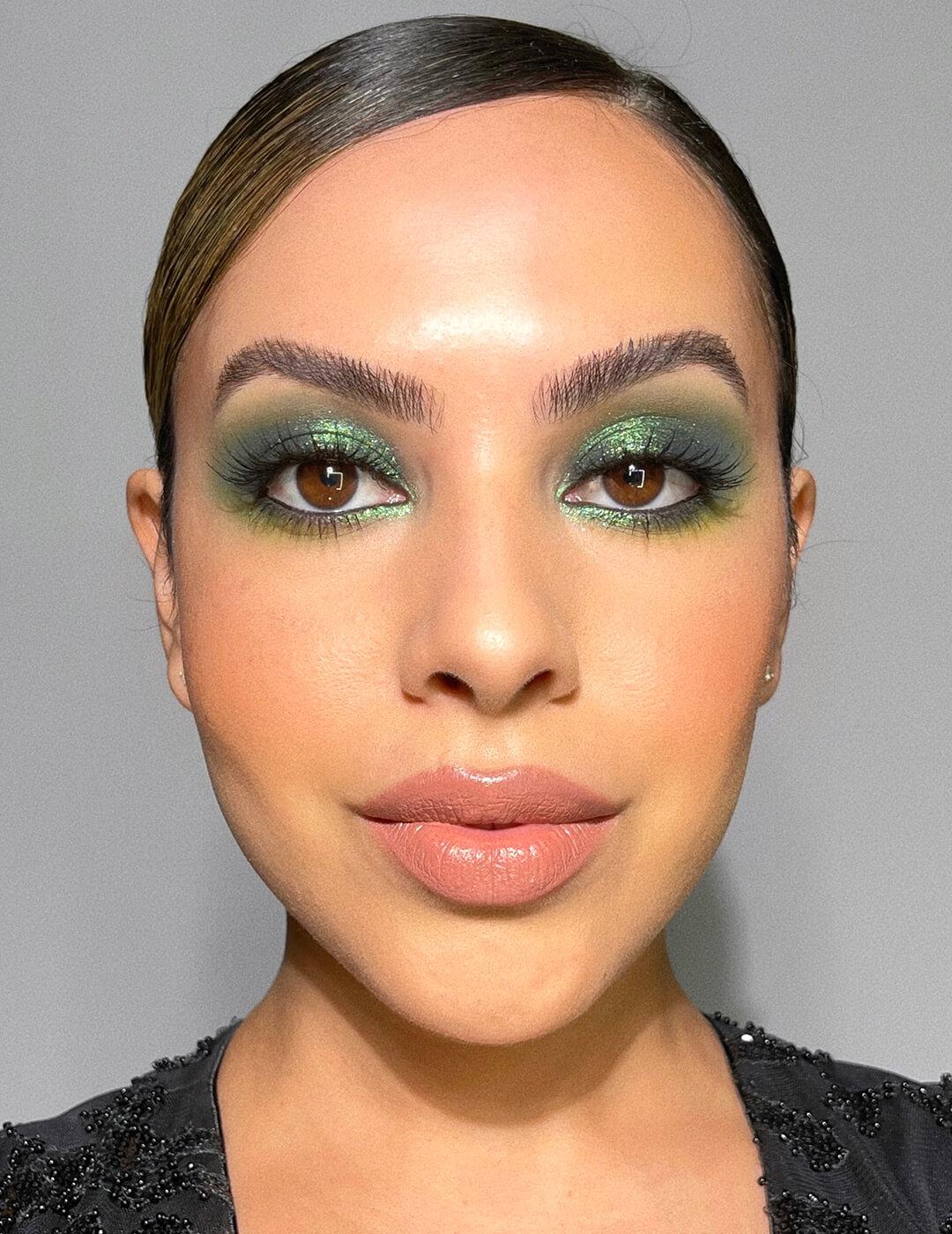 A close-up photo of a woman wearing green metallic eyeshadow with nude to pink lipstick