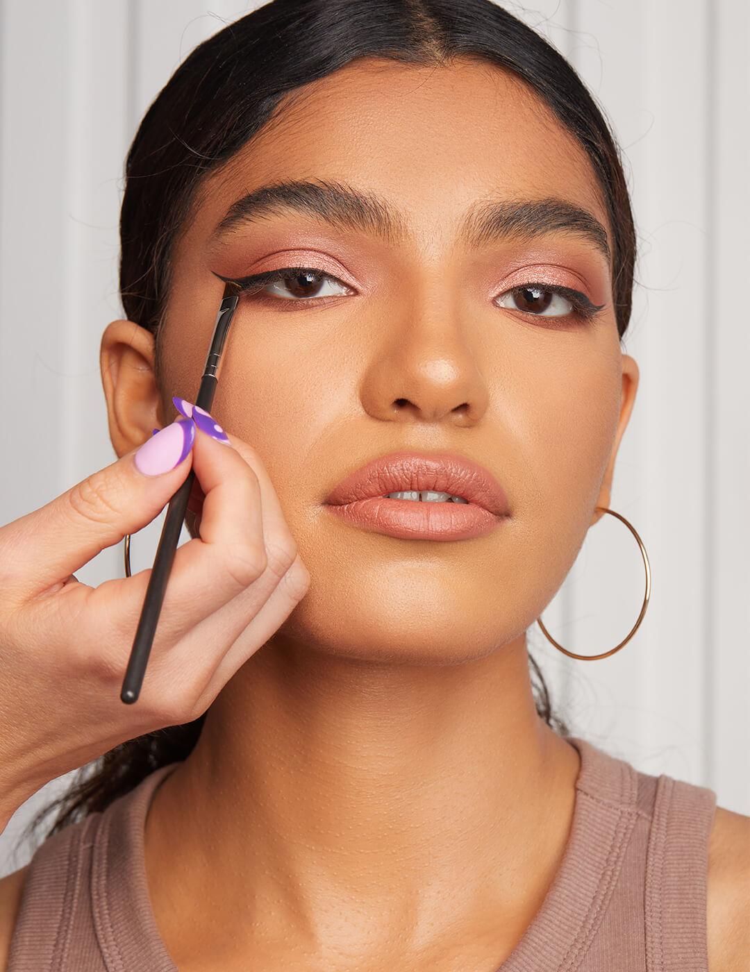Makeup artist creating a winged eyeliner look on a model using a makeup brush