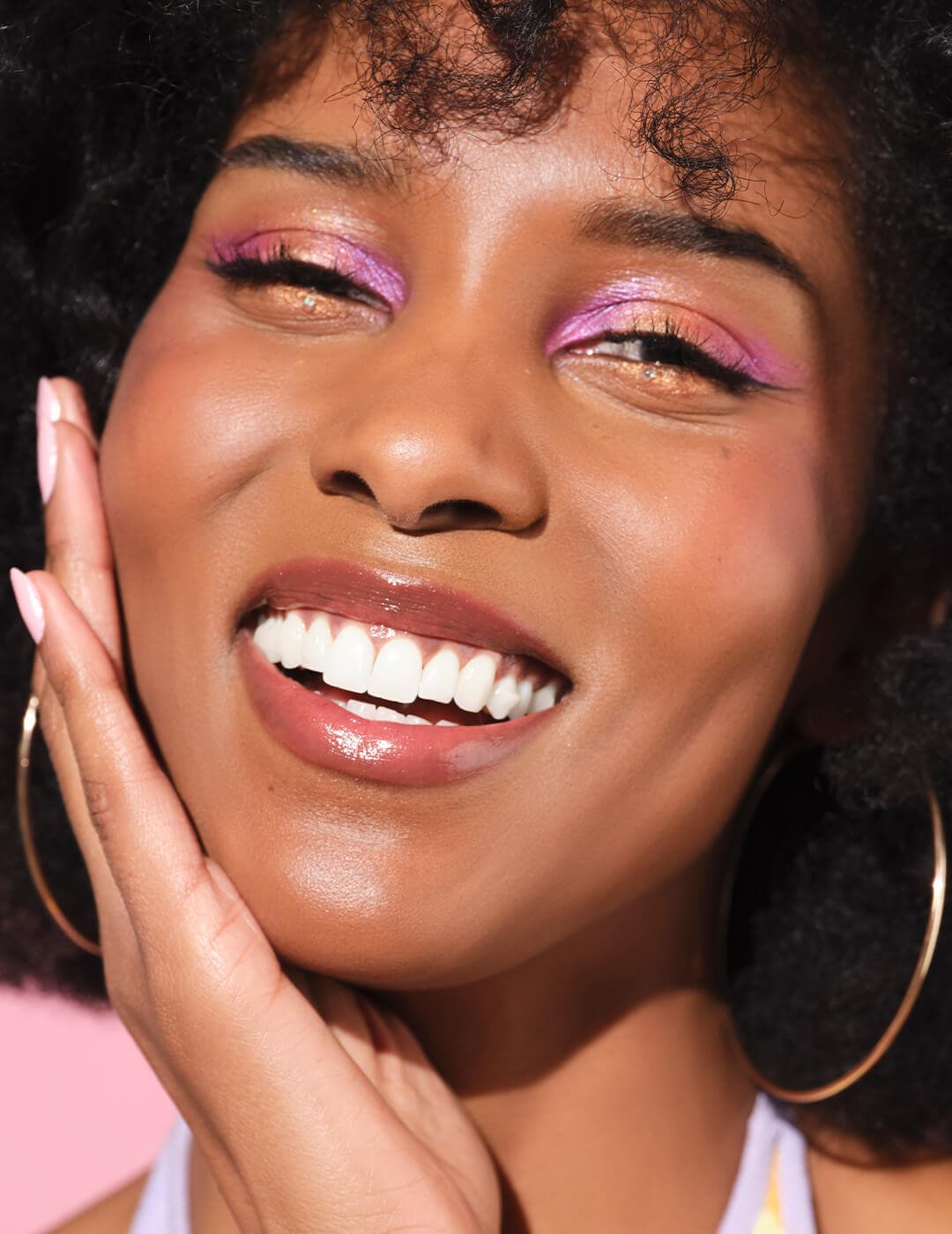 Close-up of a smiling model with shimmery pink and orange eyeshadow makeup look