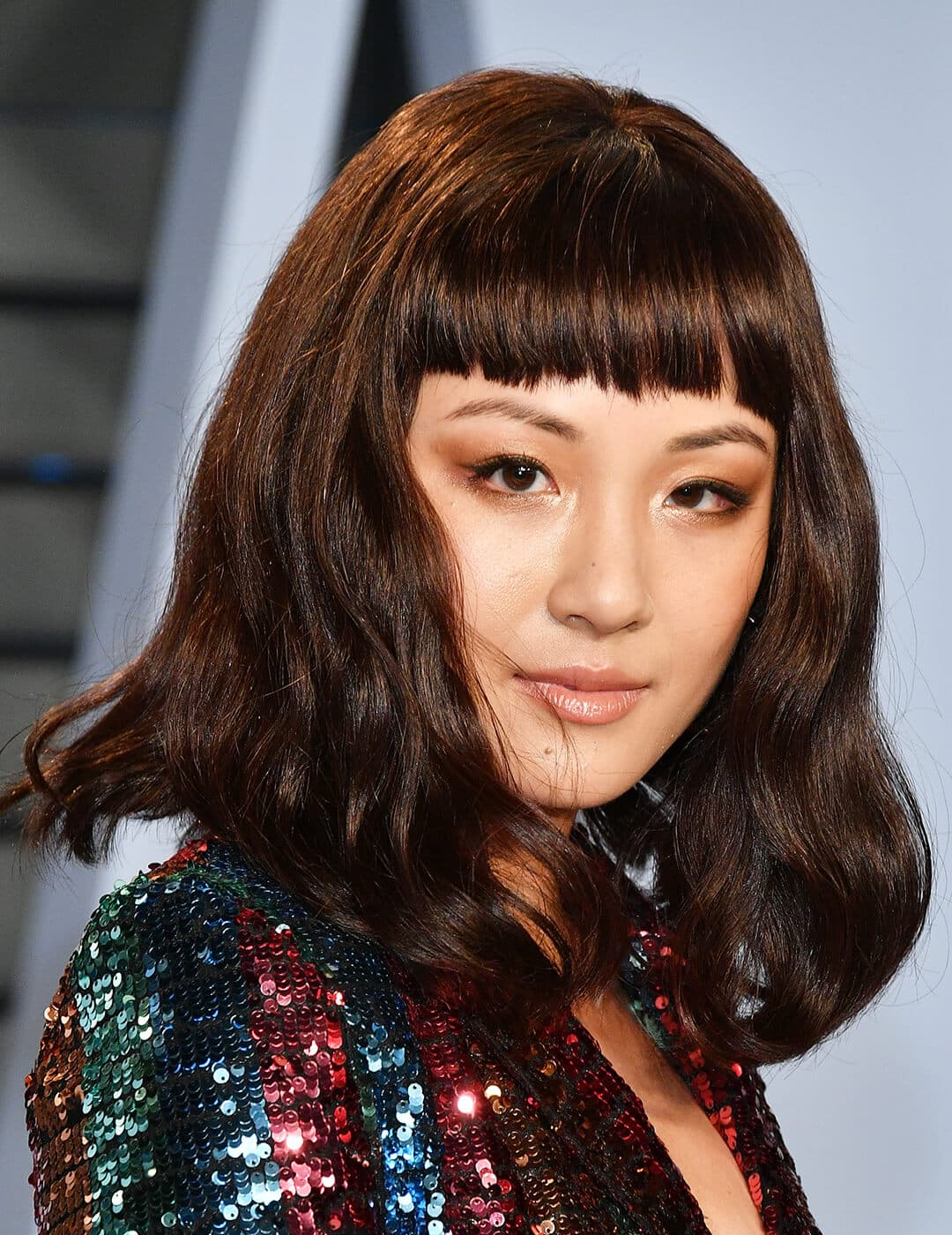 Constance Wu looking chic in a wavy hairstyle with bangs and colorful sequined dress