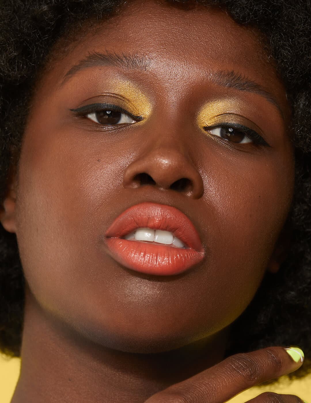 Close-up of a Black model rocking a gold inner corner eye makeup look and orange lips