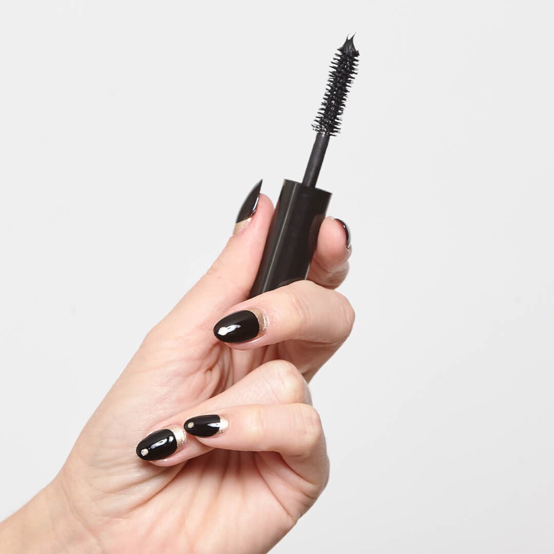 Image of model's hand with black and gold nail art mani holding a mascara wand with mascara product