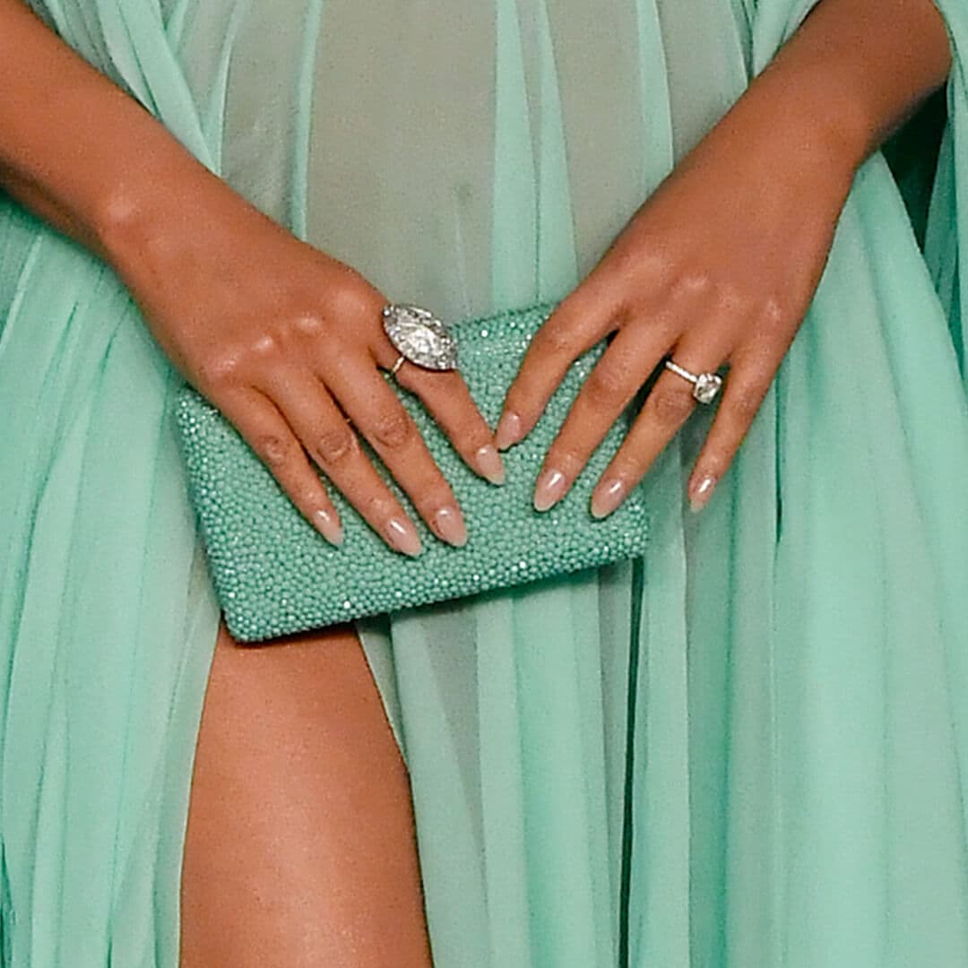 Close-up of Chrissy Teigen's hands with nude nail polish holding a mint green bejewelled purse against her sheer mint green dress
