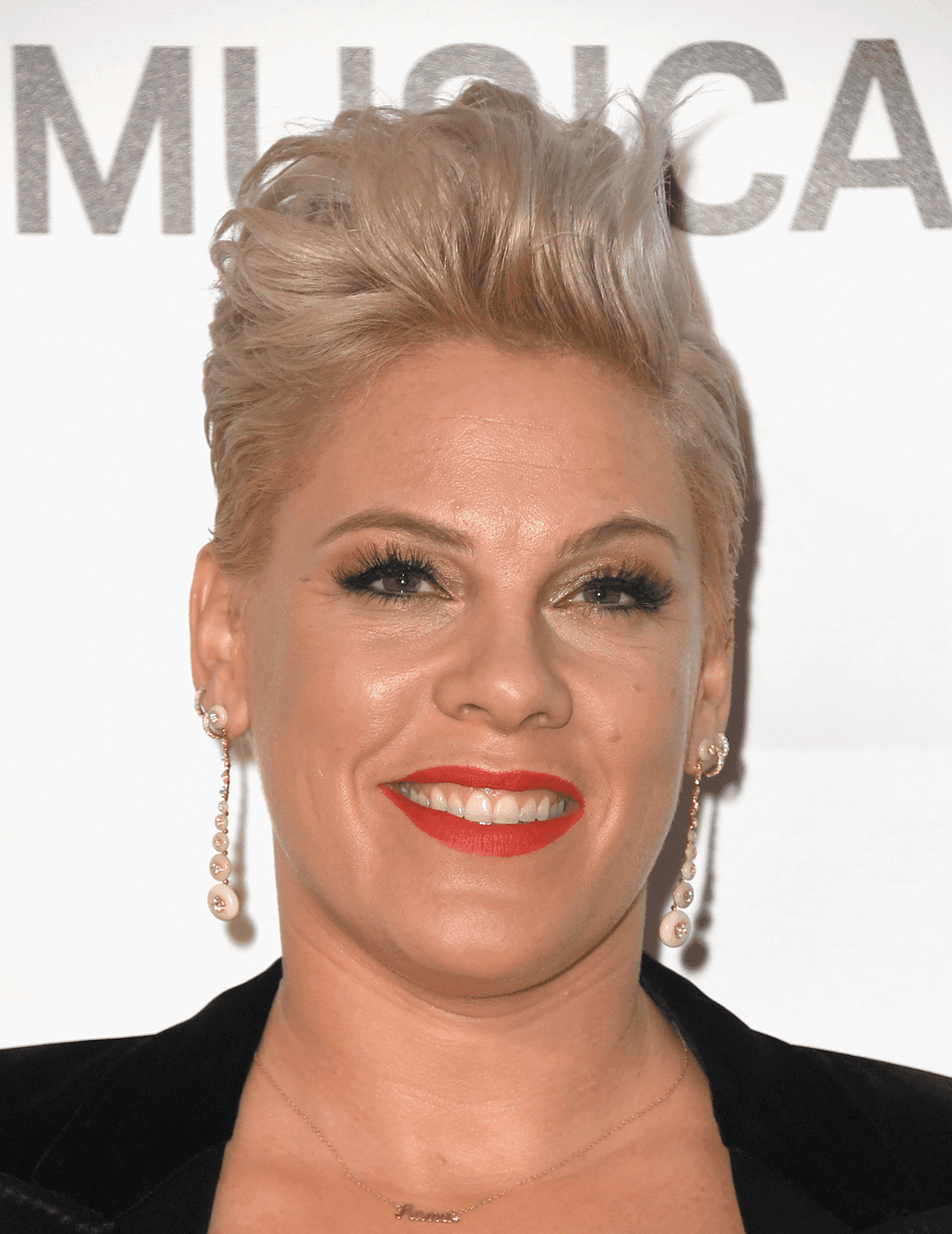 Pink rocking a black suit, gold dangling earrings, bold lip makeup look and faux hawk hairstyle