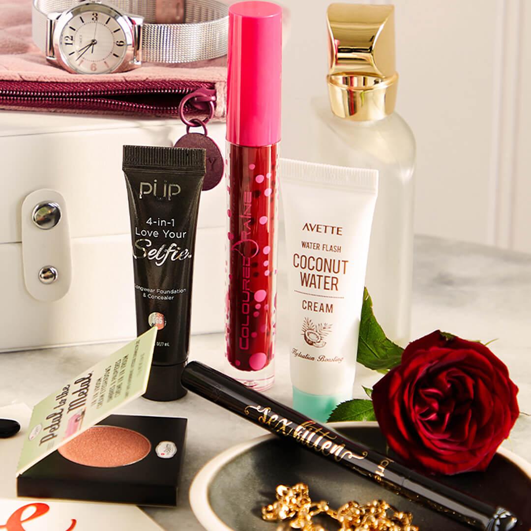 Beauty and makeup products from various brands scattered on marble top with ceramic bowl, rose flower, silver watch, and white makeup bag