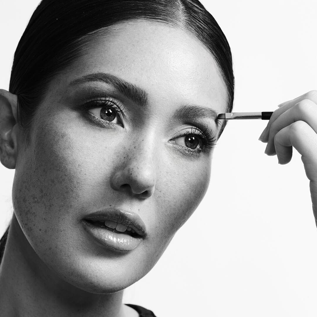Black and white portrait of a beautiful model applying brow product with a brush