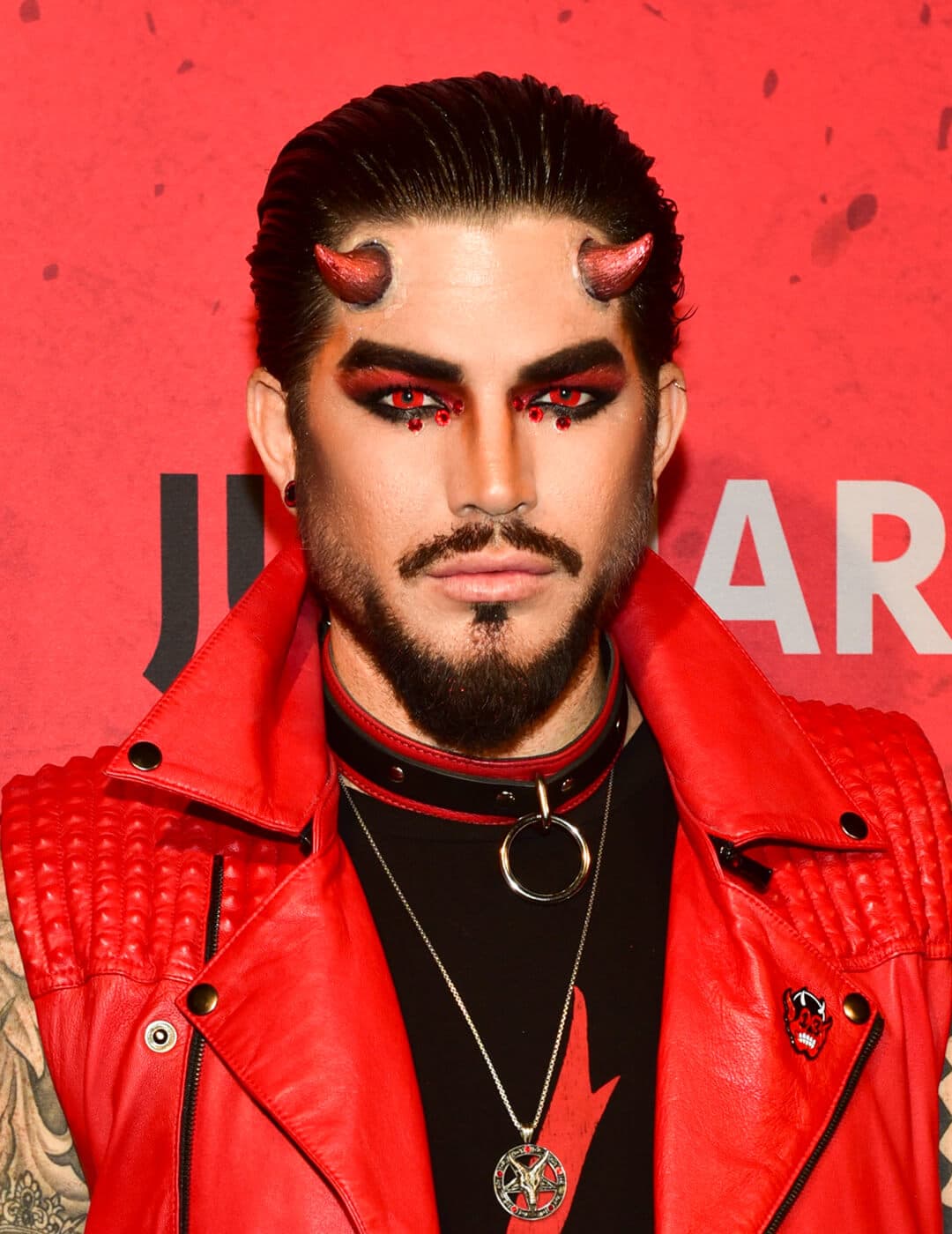 Adam Lambert dressed up as a rock star devil in red leather sleeveless jacket with matching horns
