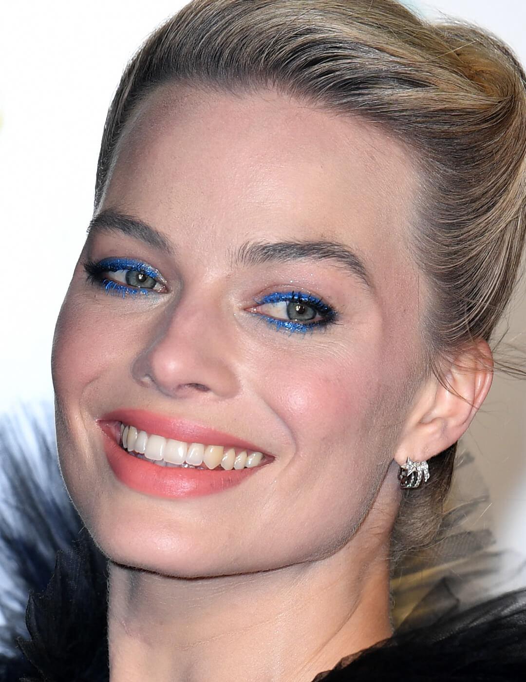 Close-up of a smiling Margot Robbie rocking a shimmery electric blue eyeliner makeup look