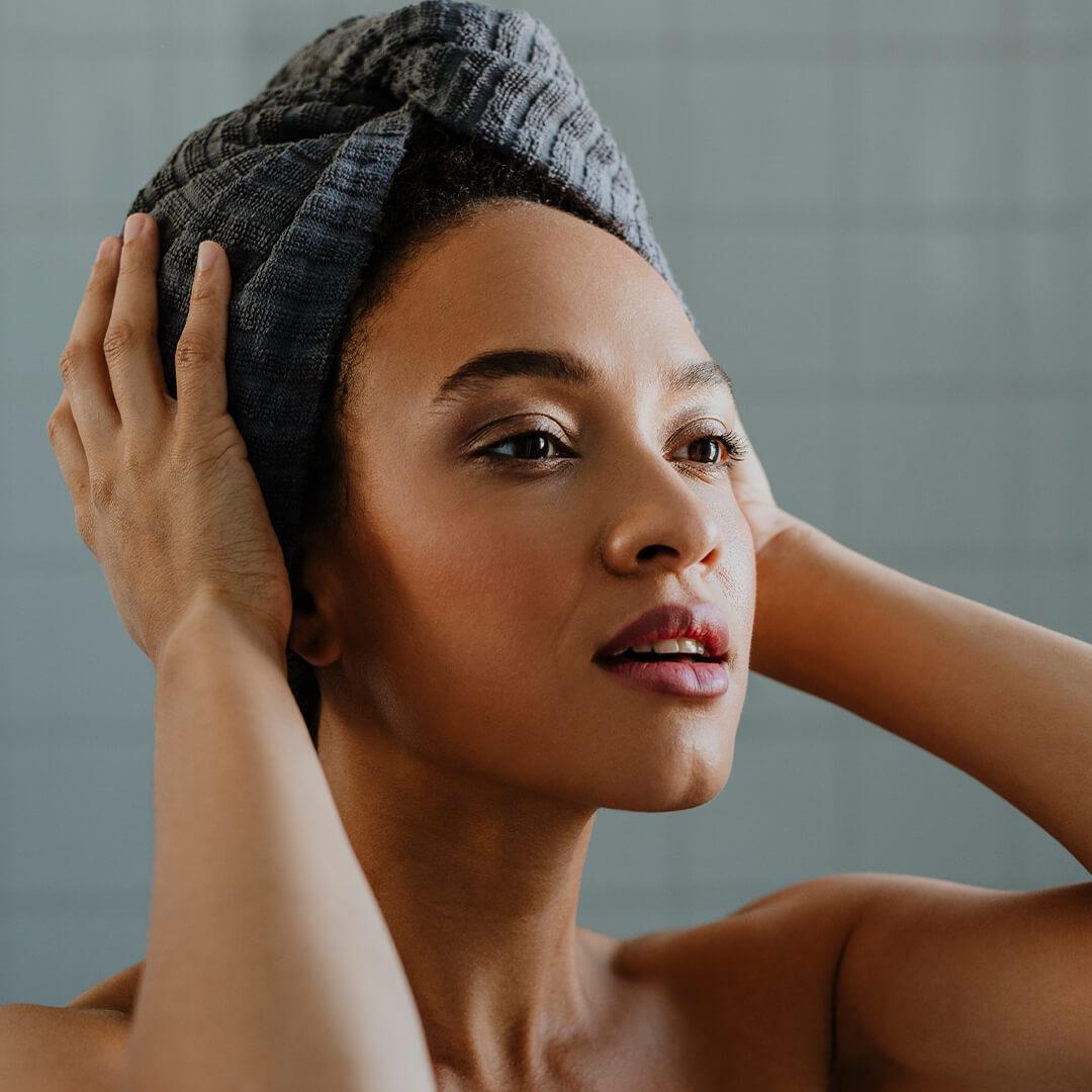 Beautiful woman with her hair wrapped in a towel posing inside bathroom