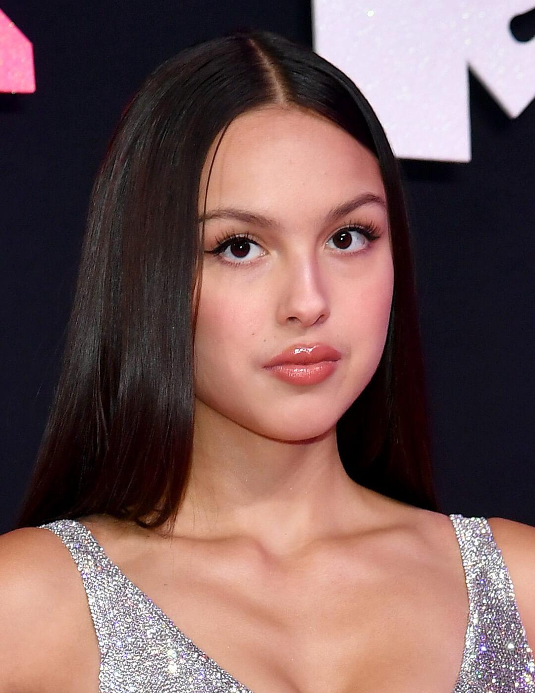A photo of Olivia Rodrigo with her sleek straight-down hairstyle wearing a silver sequins against black background