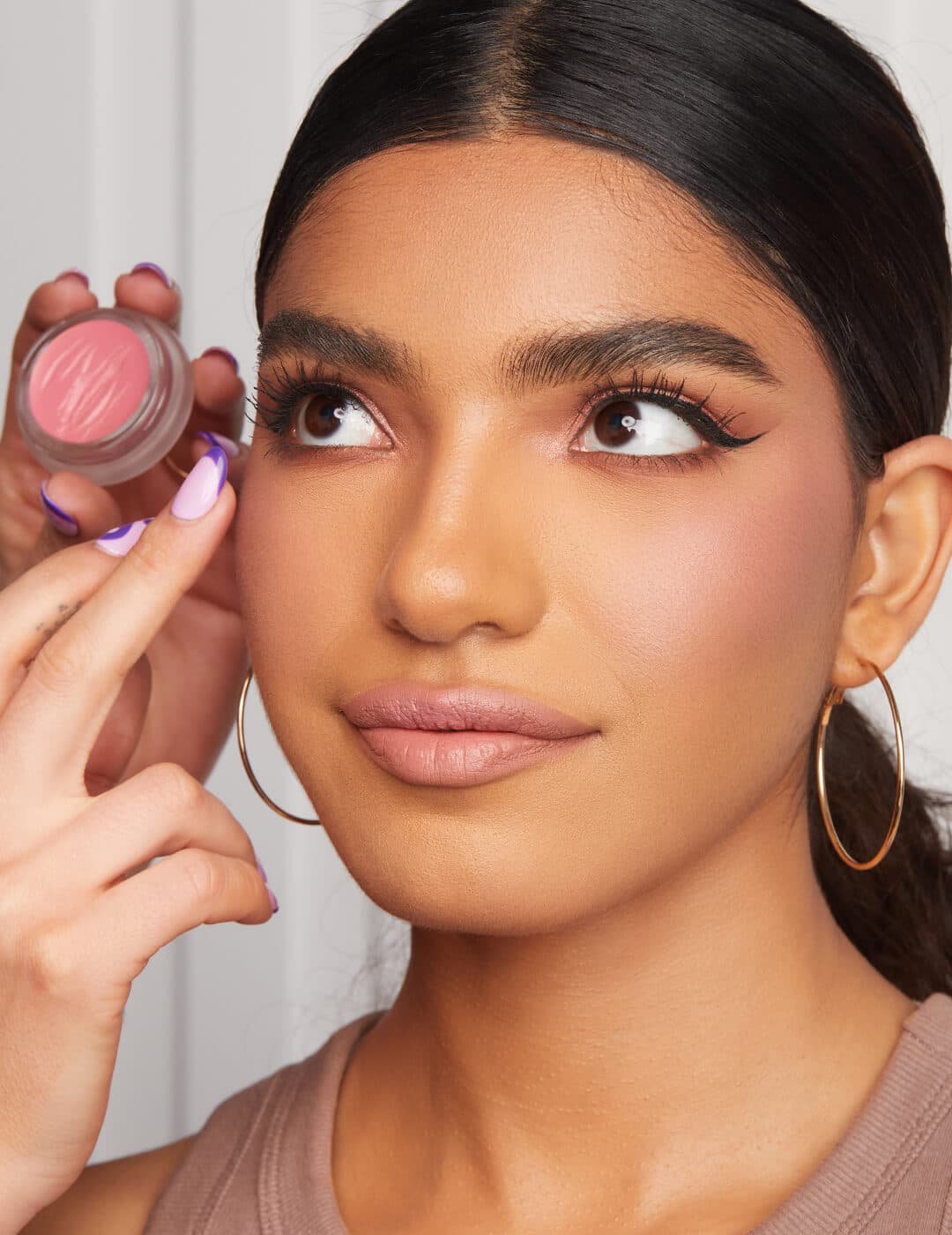 Makeup artist's hands applying cream blush on a model's cheek