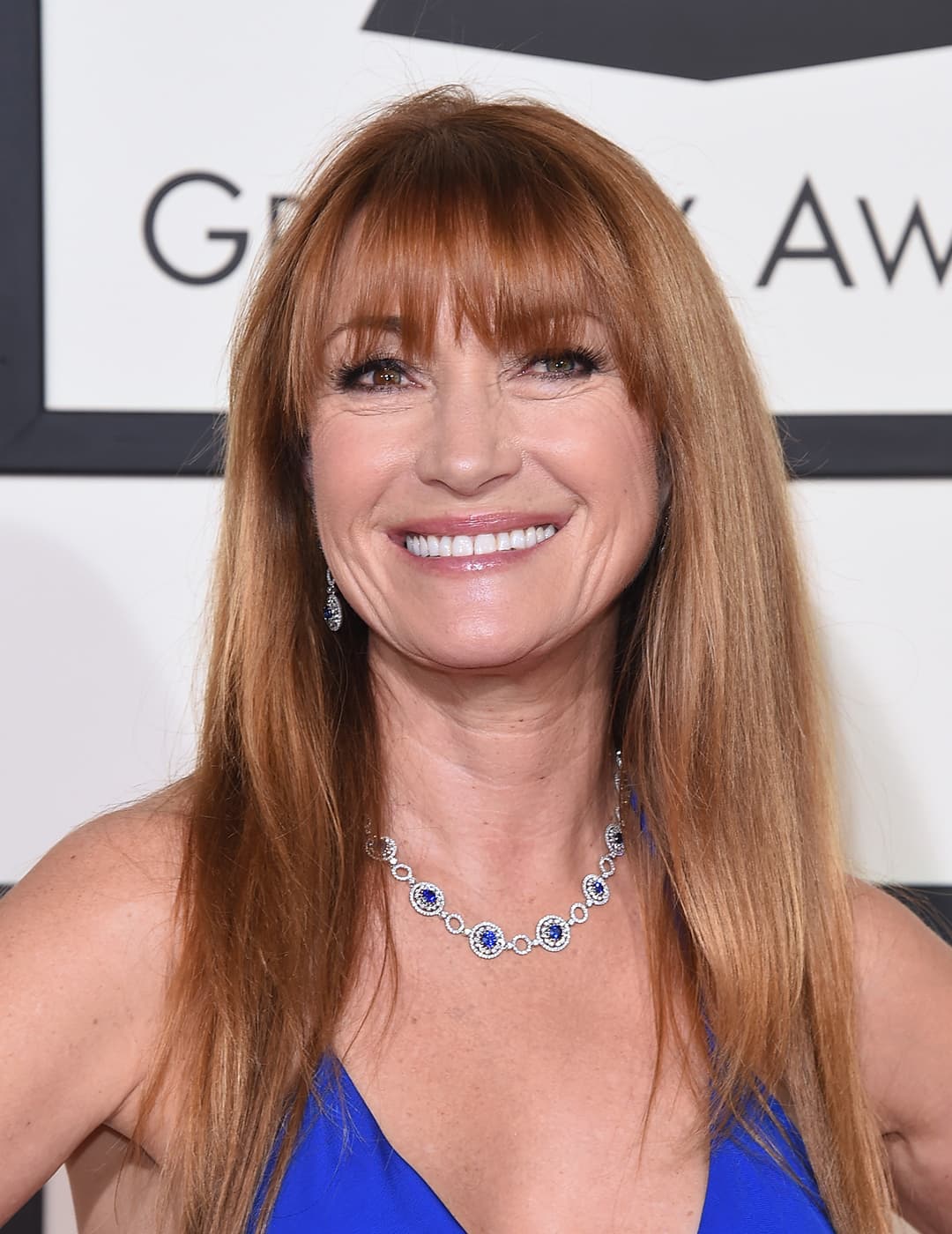 A photo of Jane Seymour with her Wispy Bangs and Long Hair wearing a blue dress and a necklace with a blue gem 