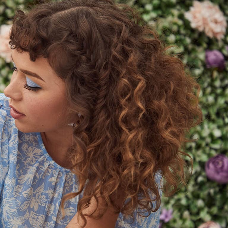 A close-up image of a curly-haired model with partly hidden braids