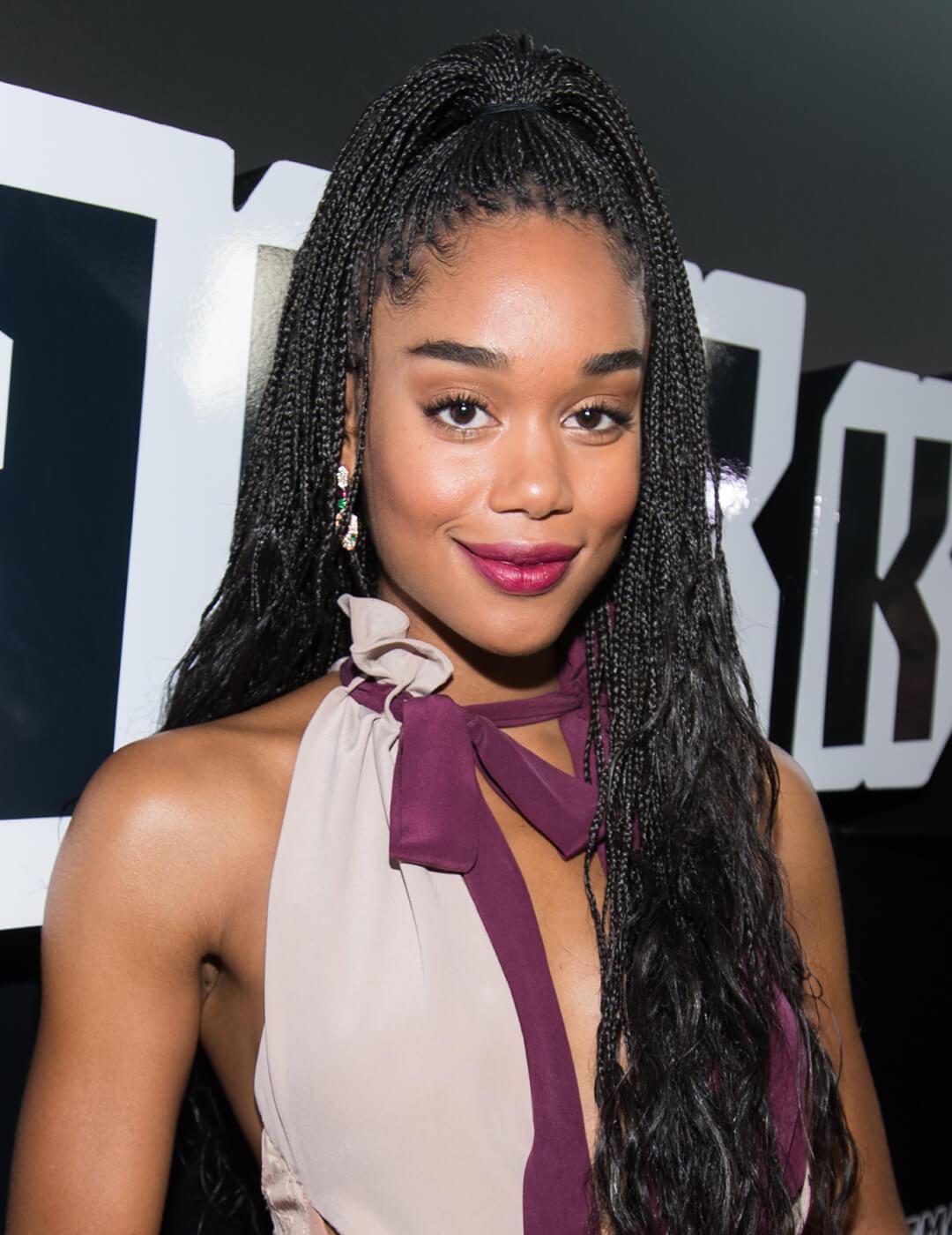 Laura Harrier rocking a Bohemian braids high ponytail hairstyle, burgundy and offwhite dress, and neutral eyeshadow makeup paired with berry lips