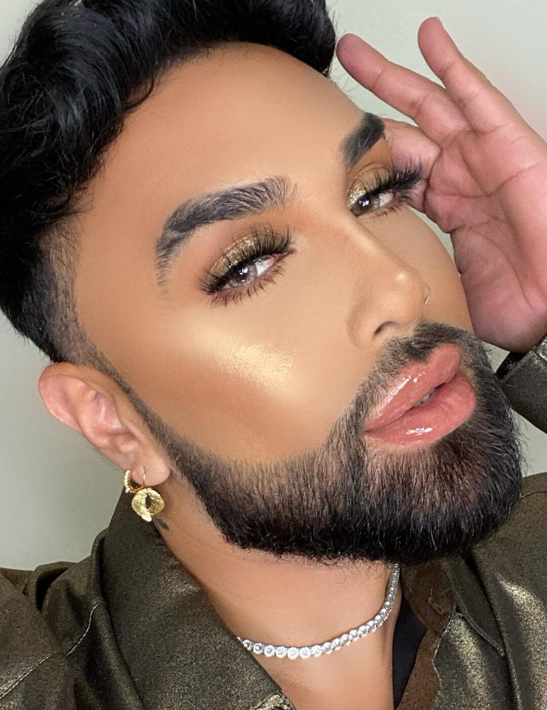 A photo of a man with defined eyebrow and clean beard and uses shiny gold eyeshadow