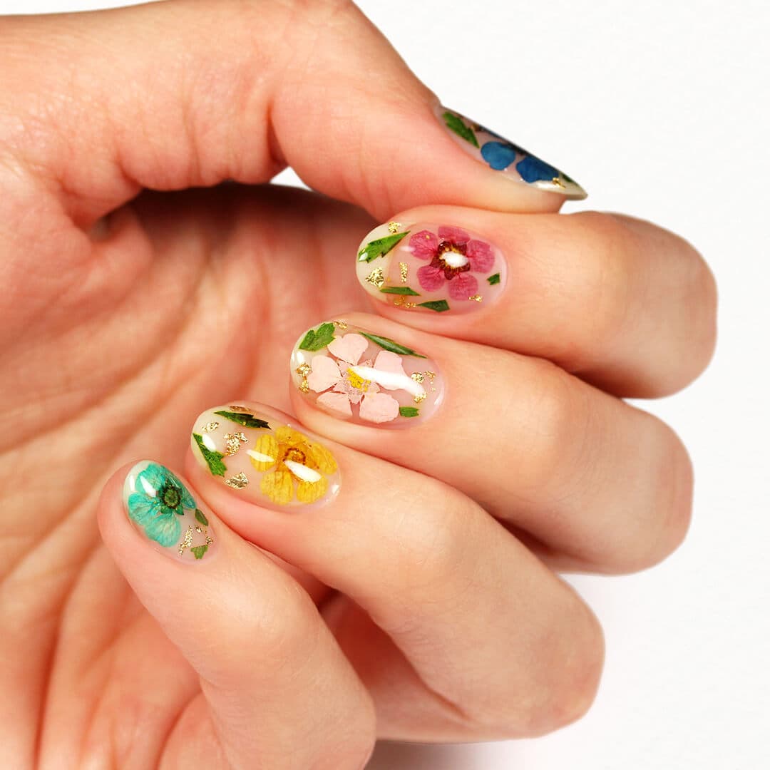 An image of a model's fingers with dried flowers and gold leaf nail art