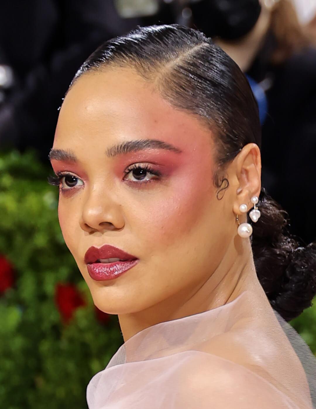 Tessa Thompson rocking a pink blush and eyeshadow paired with a neat low-ponytail hairstyle