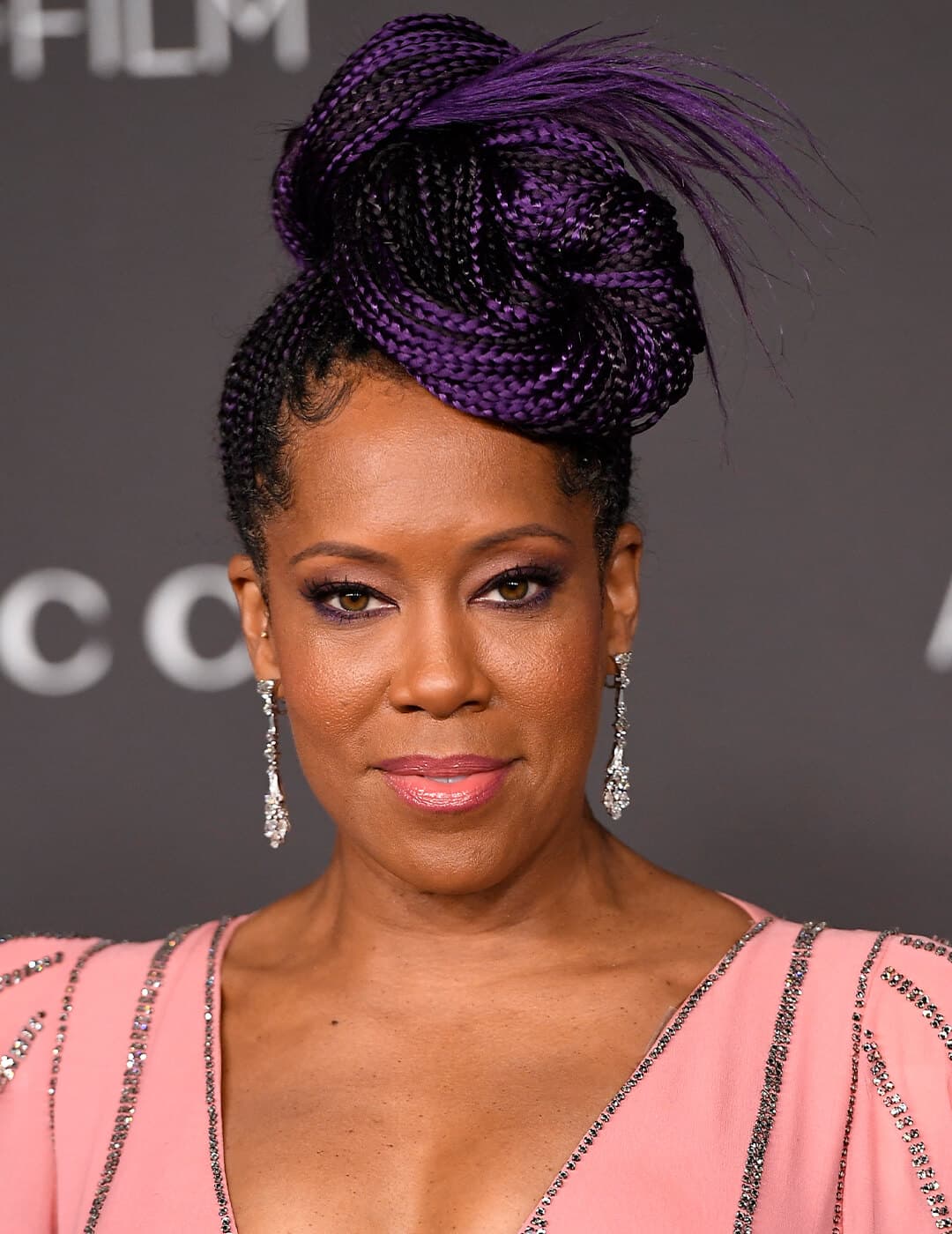Regina King rocking a purple braided updo hairstyle, smoky eyeshadow makeup, silver dangling earrings, and pink and silver sequins dress