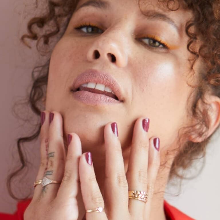 An image of a curly-haired model wearing mauve nail polish holding her lower jaw