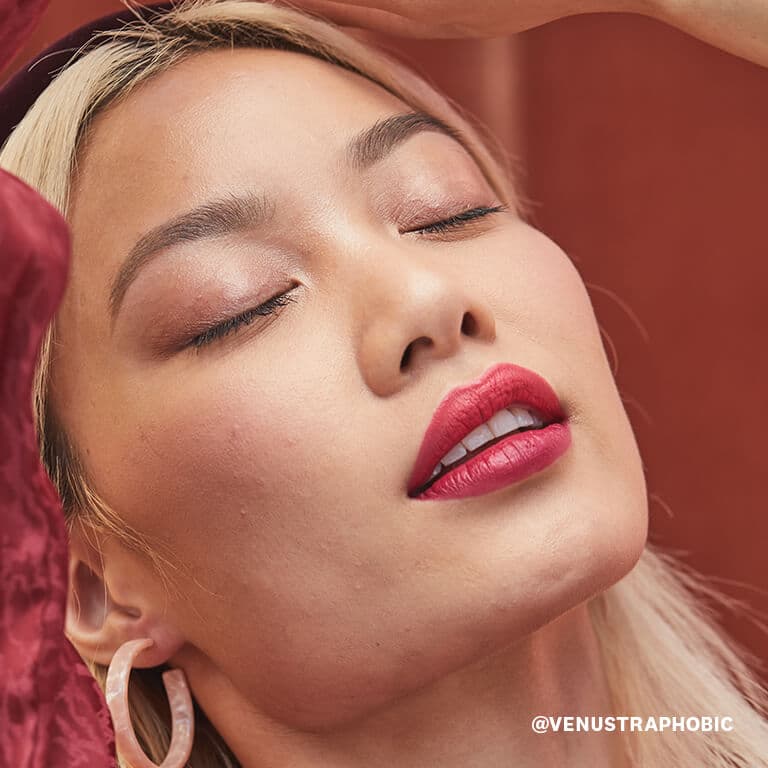 A closeup image of a model wearing champagne colored eyeshadow and bold rose lipstick