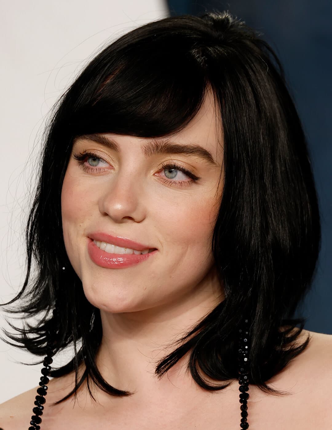 A photo of Billie Eilish with her black medium-length bob cut while looking and smiling sideways