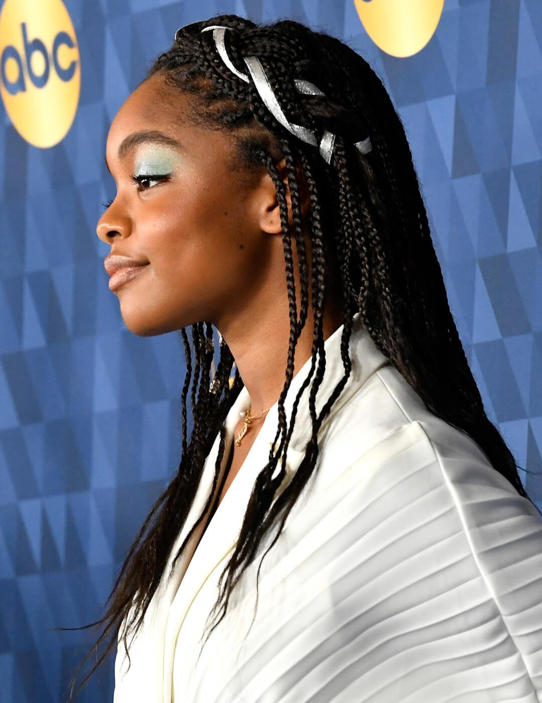 Marsai Martine looking glam in a textured, white dress, light blue green eyeshadow look, and braided hairstyle woven with silver ribbon