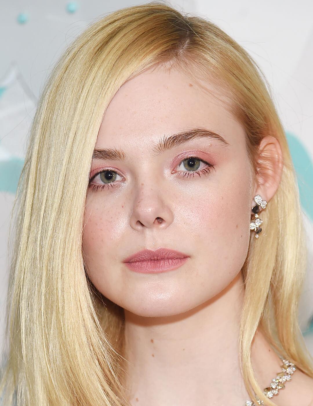 An image of Elle Fanning looking fierce in her pink eyeshadow and lipstick with hair tucked in on one side
