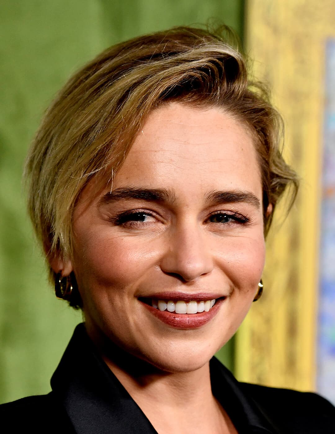 Close-up of Emilia Clarke smiling and rocking a neutral makeup look and long pixie cut hairstyle