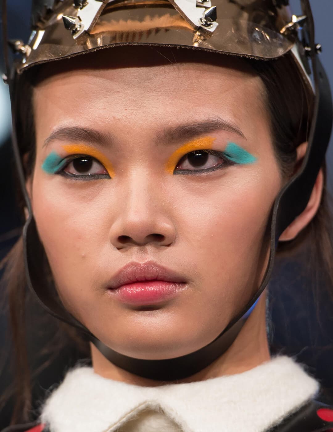 Model wearing a brown leather head piece and blue and orange eye makeup