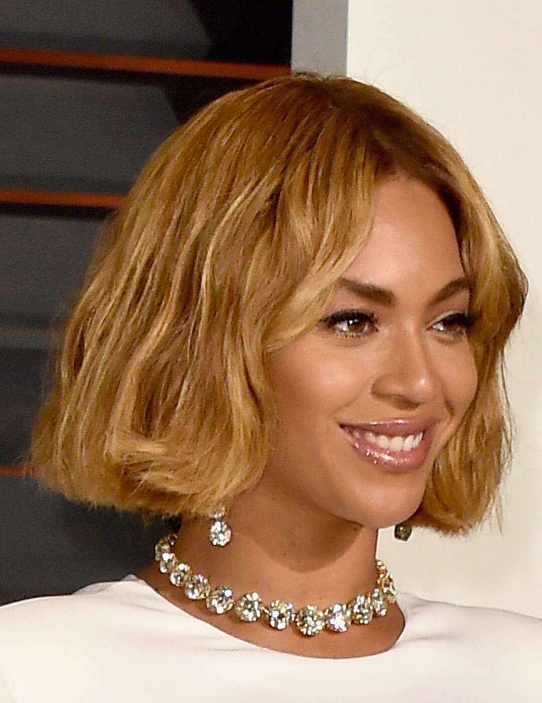 An image of Beyonce beautifully smiling with her glossy, nude lipstick accentuated with a white-gold necklace and earring