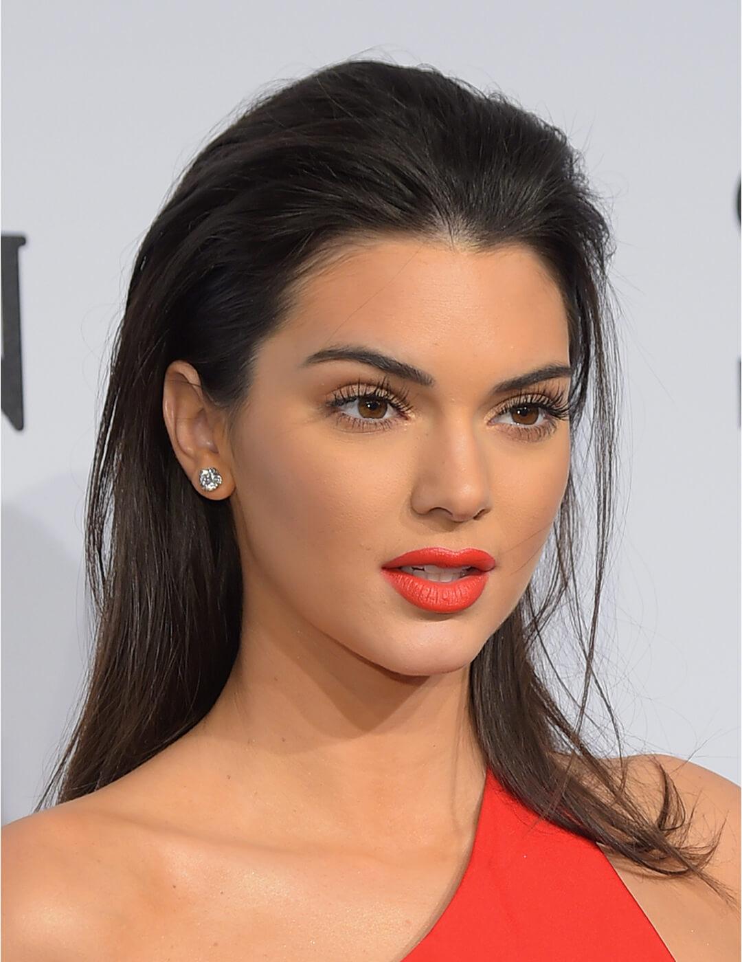 Close-up of Kendall Jenner rocking a neutral eye makeup paired with bright coral lipstick and a slicked back hairstyle