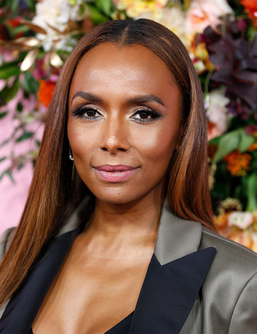 Janet Mock in a grey suit smiling against flowers background