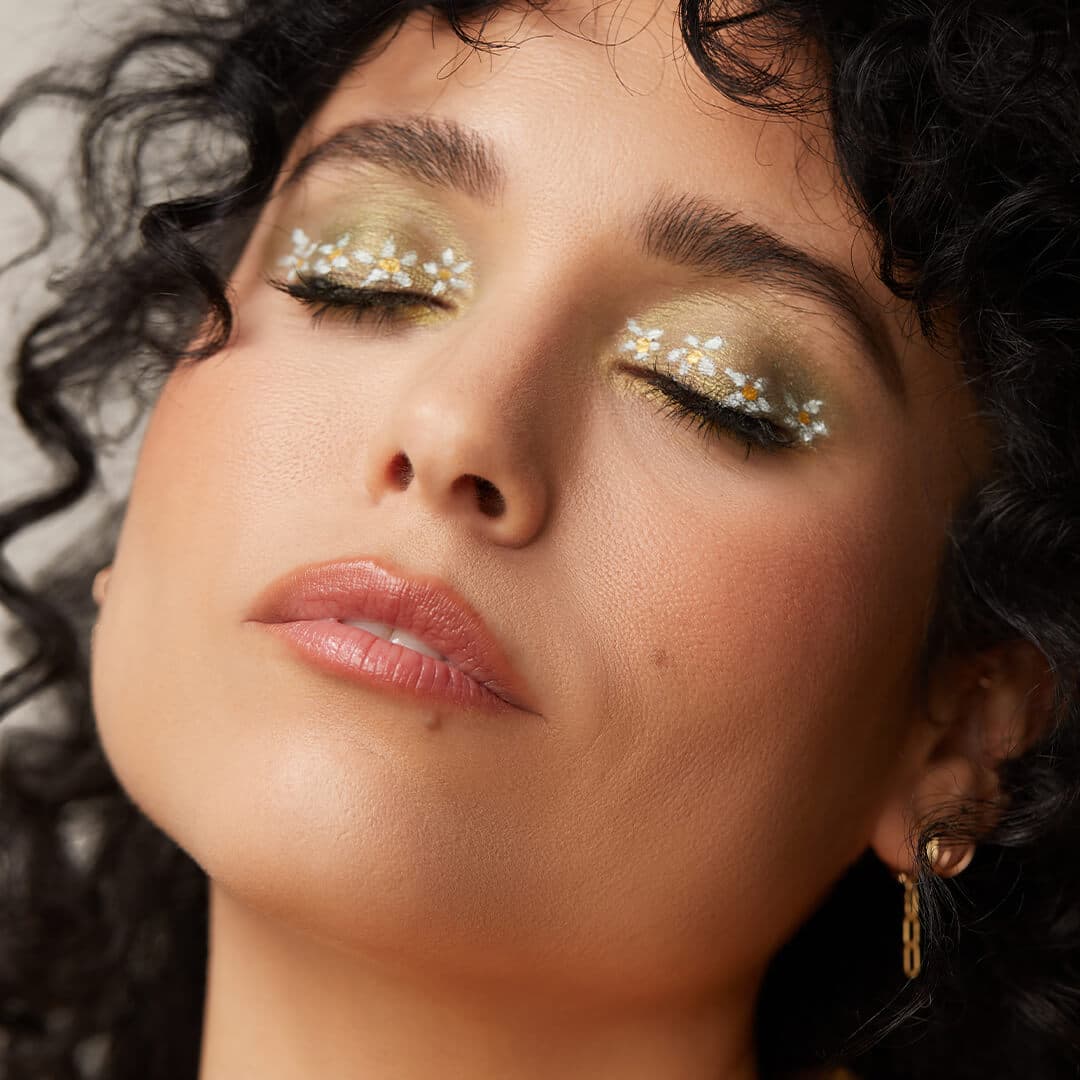Close-up of a model posing and rocking a green eyeshadow and white daisies makeup look