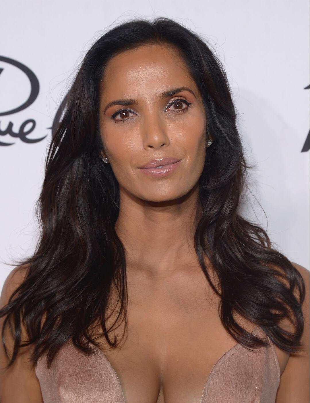 Padma Lakshmi posing in a shimmery nude dress with a beach wave hairstyle