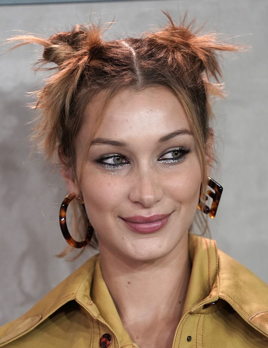 A photo of Bella Hadid with space buns wearing a yellow jacket and Fendi earrings