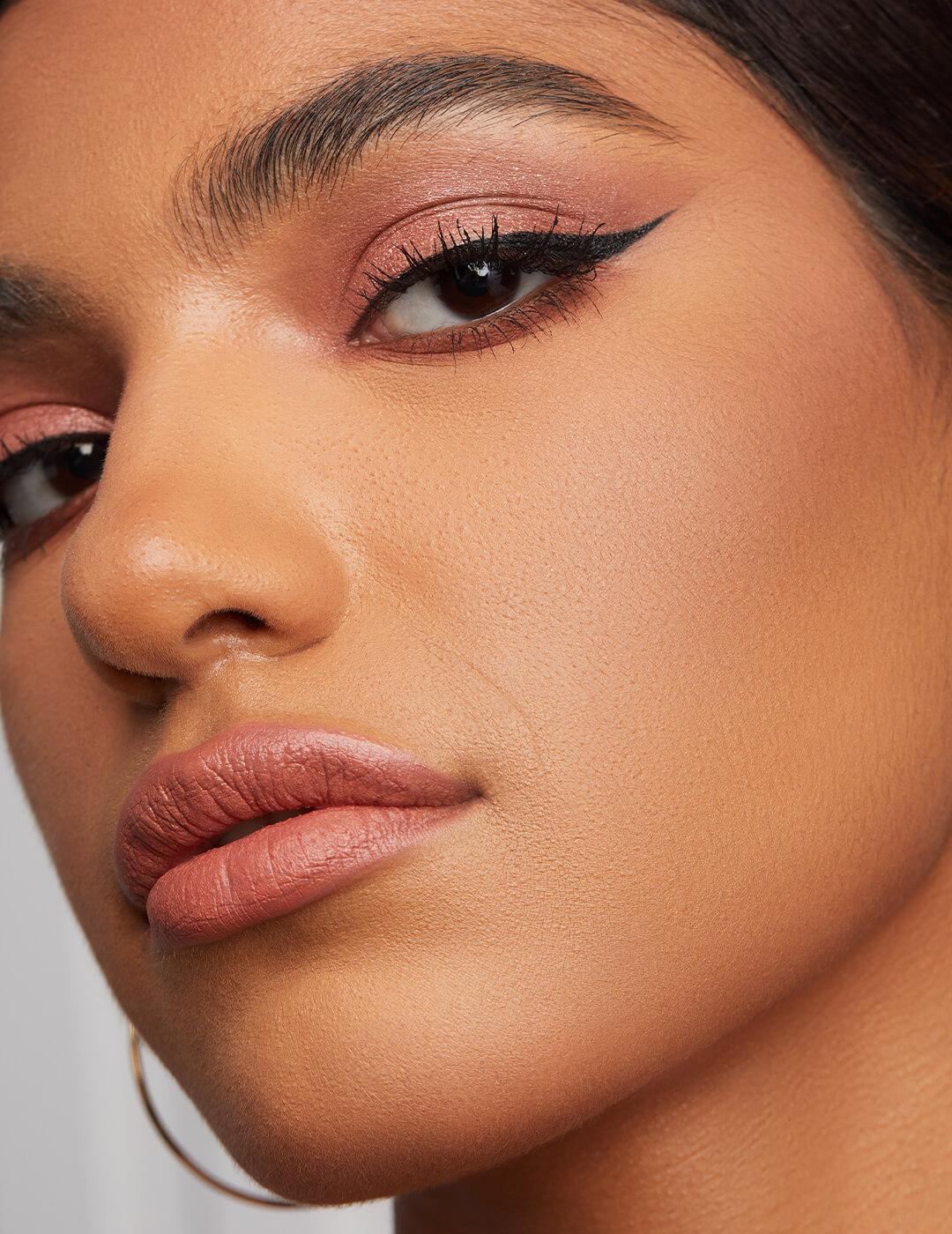 Close-up of a model rocking shimmery a rose gold eyeshadow and winged eyeliner look and nude pink lips
