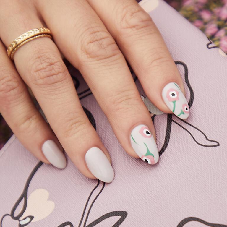 Close-up of a model's hand with hand drawn poppies nail art holding the April 2020 IPSY Glam Bag