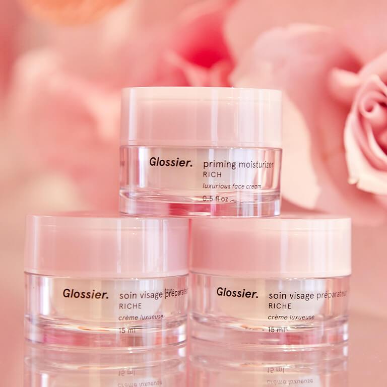 An image of three GLOSSIER Priming Moisturizer Rich stacked with roses as backdrop