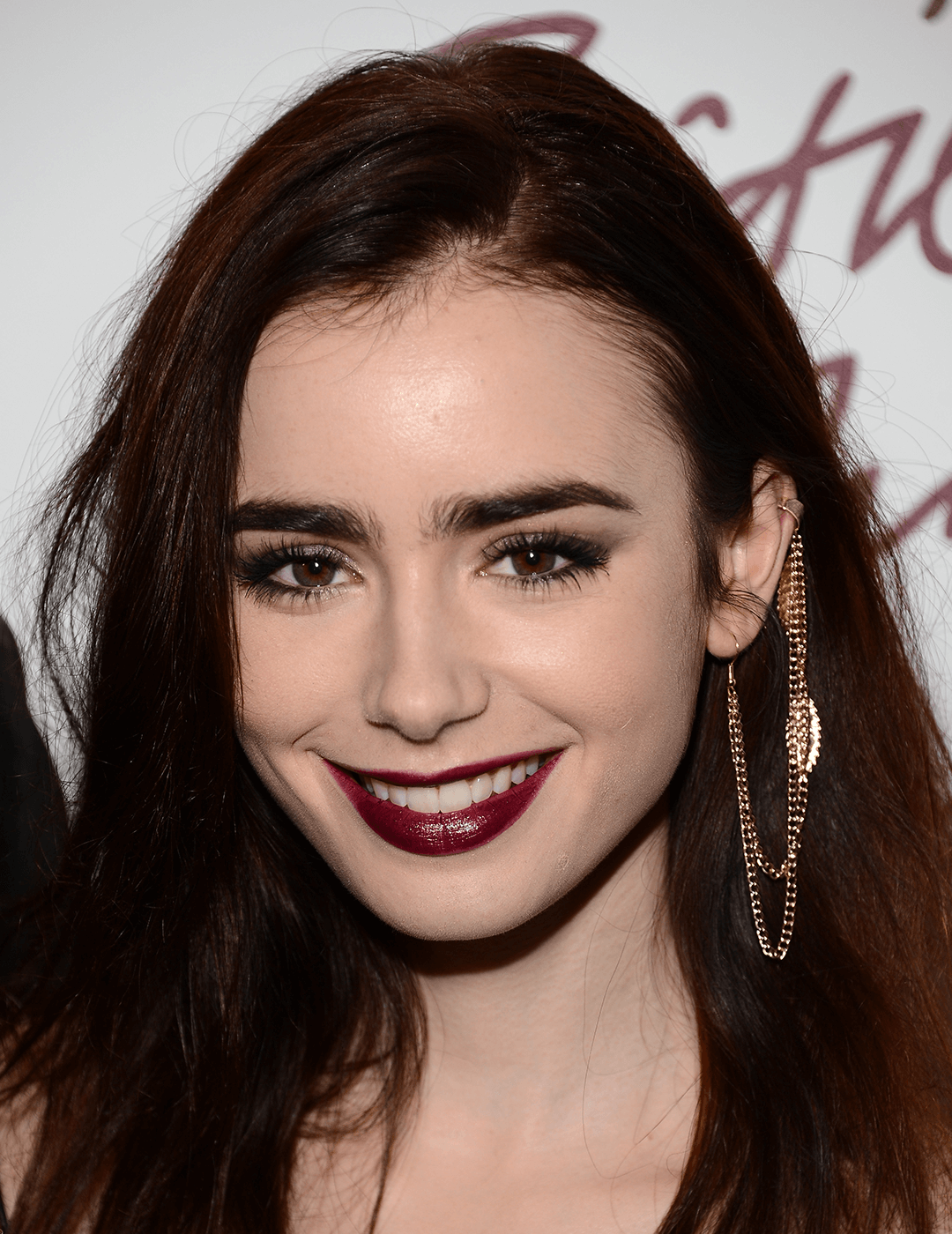 Close-up of a smiling Lily Collins rocking a glossy, dark berry lipstick look