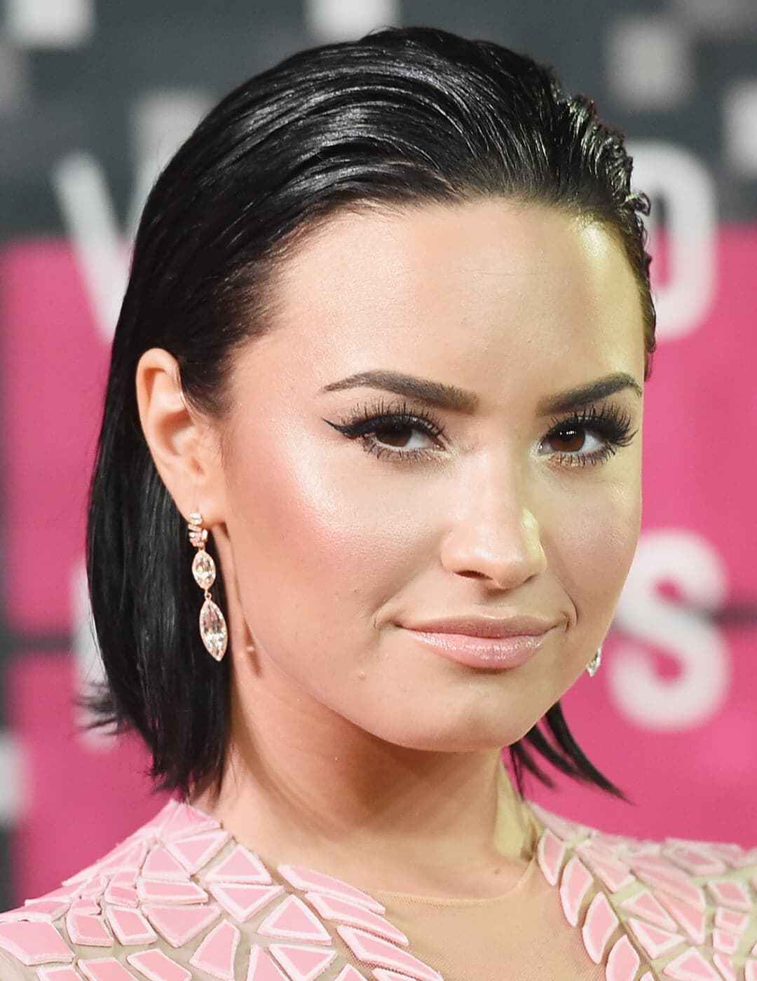 A photo of Demi Lovato showcasing her combed back, dewy look bob hair paired with an elegant earring 