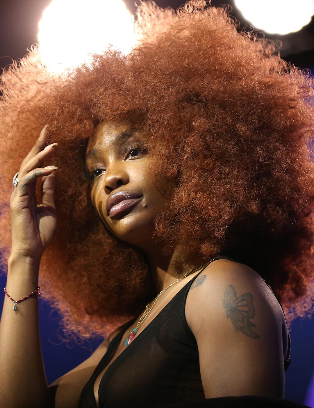 A photo of SZA with a mocha copper afro hair and wearing a black dress