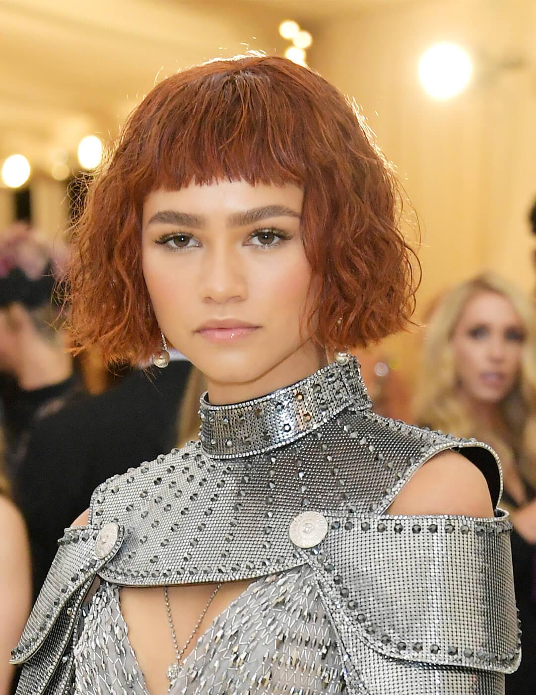 A photo of Zendaya with a Joan of Arc inspired look with super deep copper textured crop hair and a custom Versace dress