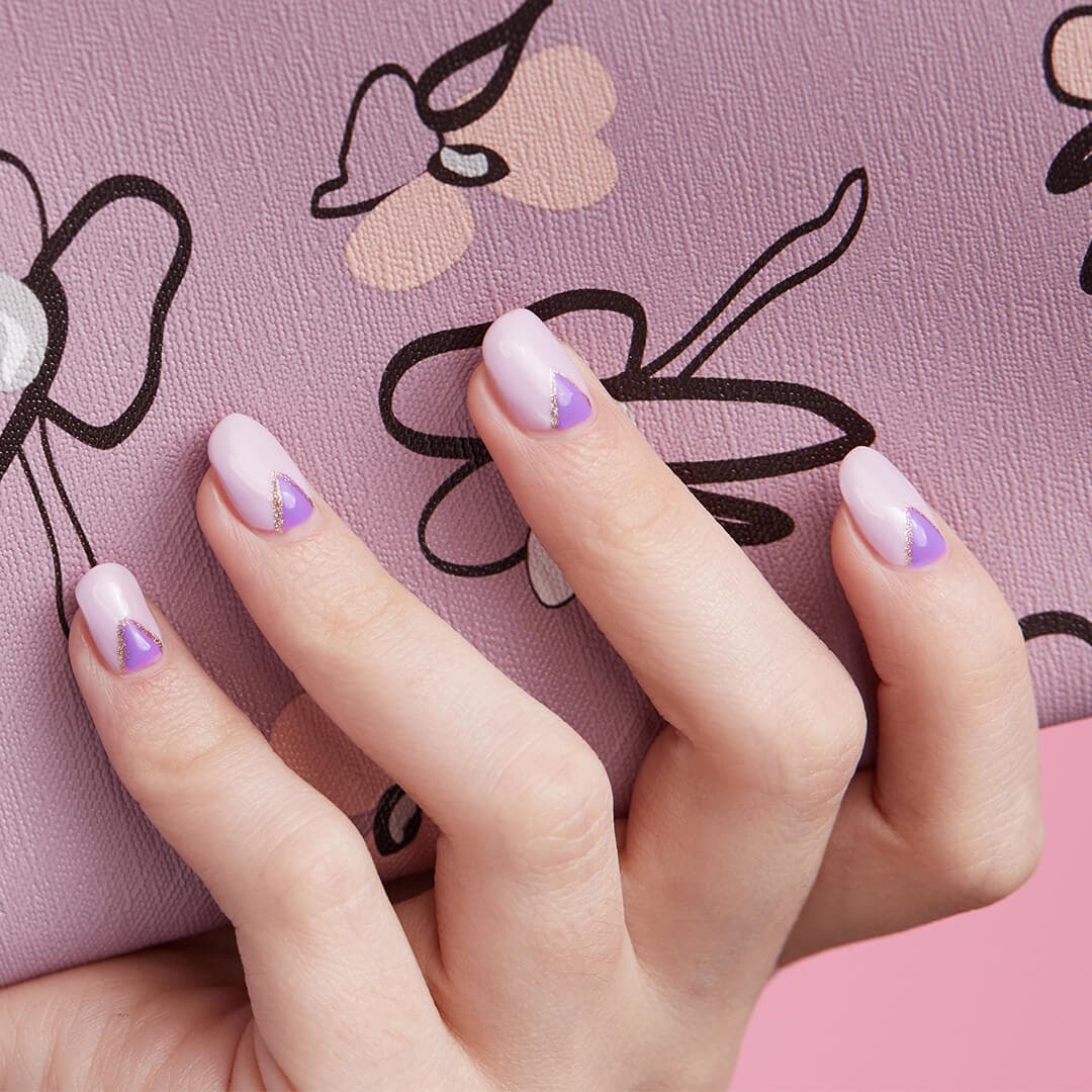 Image of a woman's hand with purple triangles nail art holding IPSY April Glam Bag