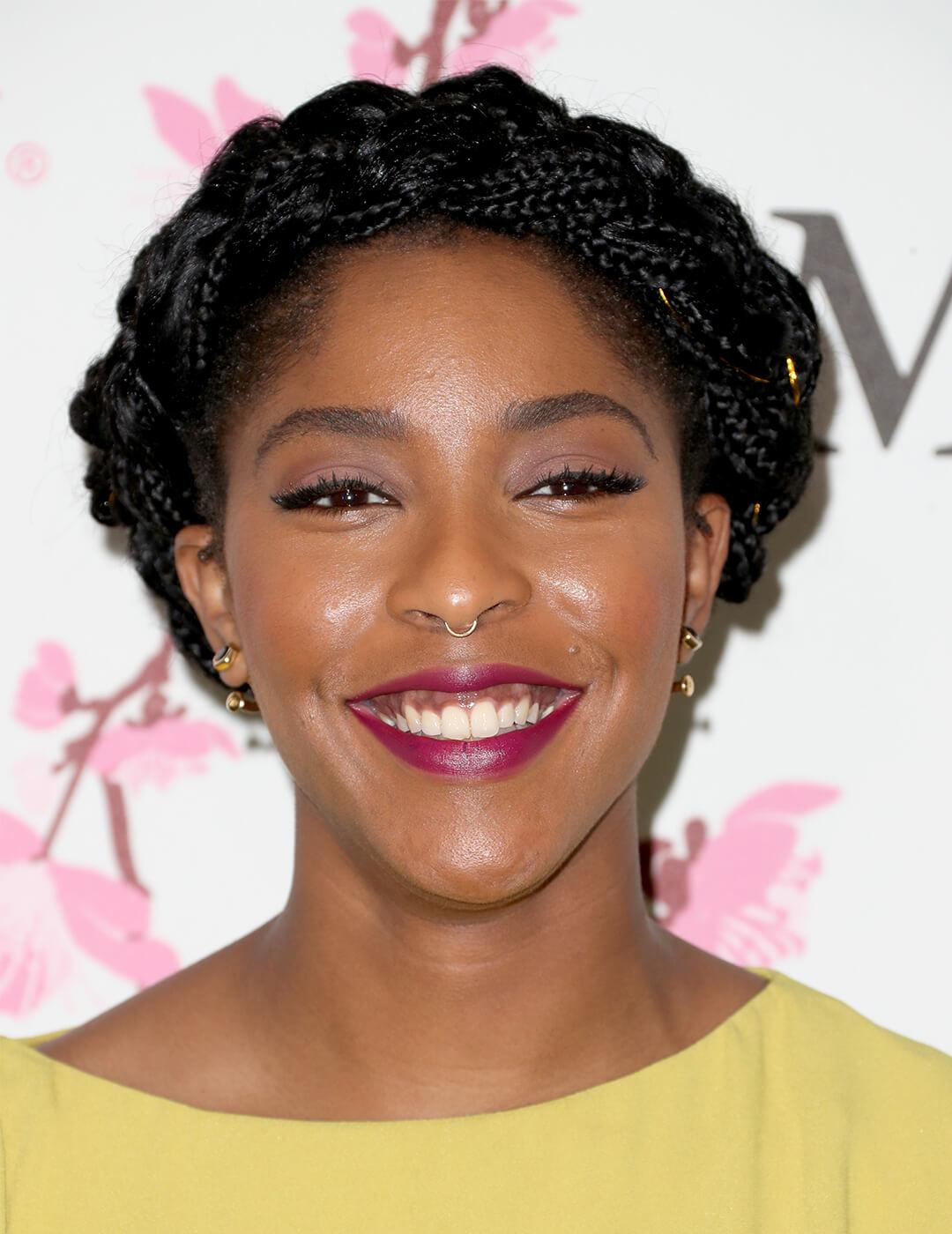 Smiling Jessica Williams rocking a yellow dress and halo braids hairstyle on the red carpet