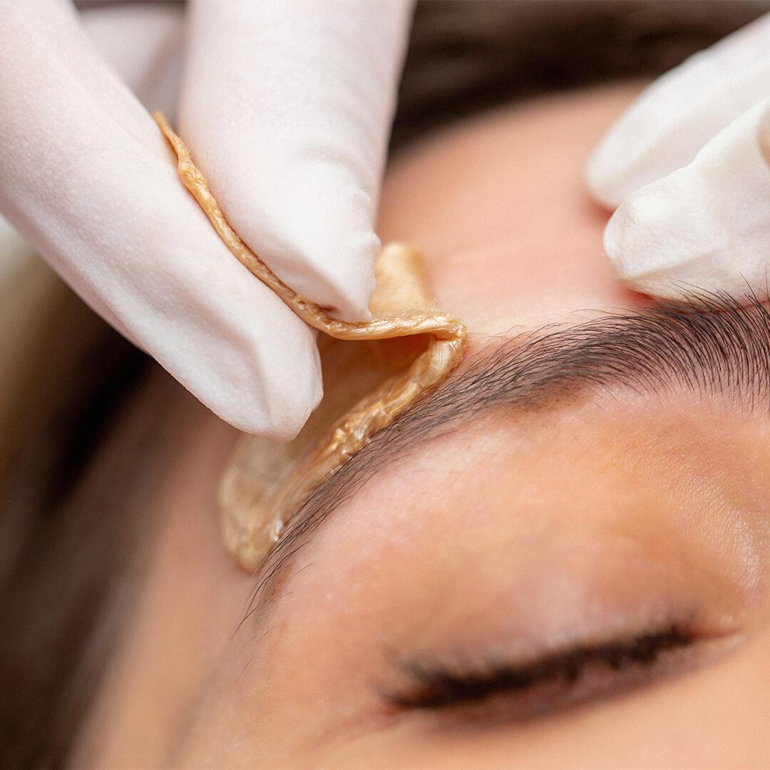 Close-up image of a woman's eyebrow being waxed