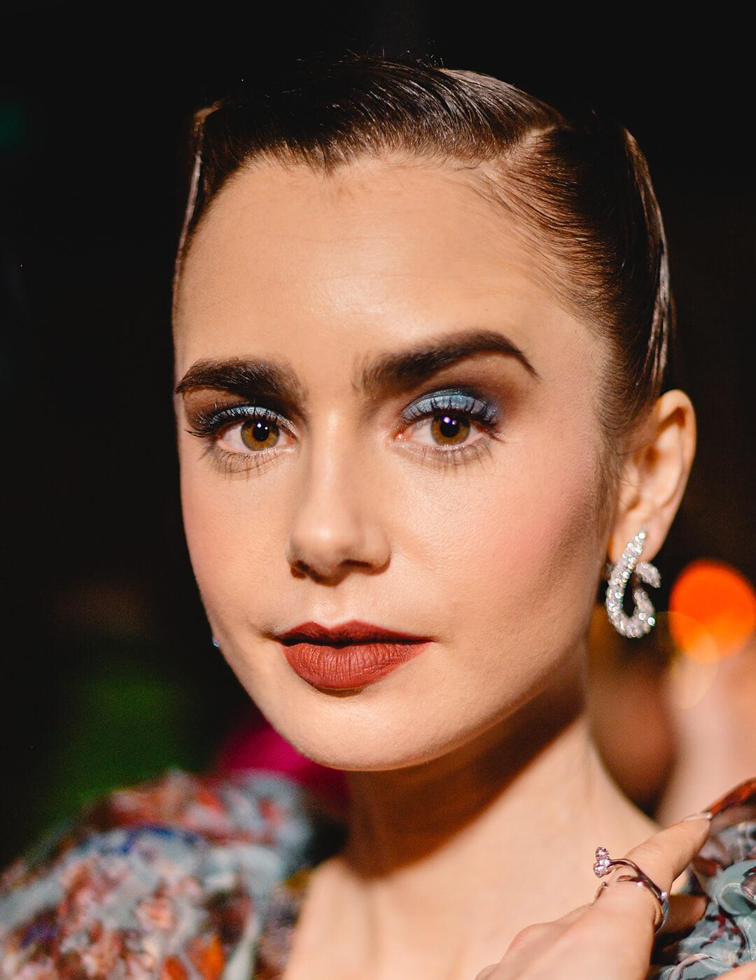 Lily Collins looking glam in a sleek hairstyle, blue smoky eyeshadow makeup look, and floral dress