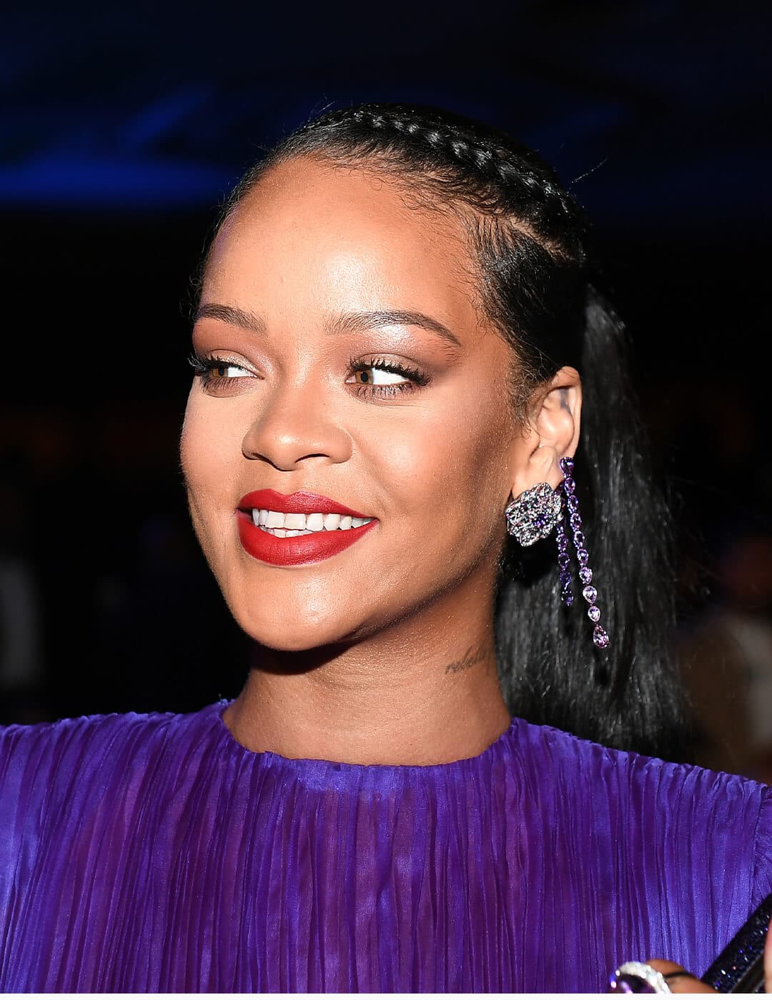 Rihanna looking glamorous in a purple dress and side braided ponytail hairstyle