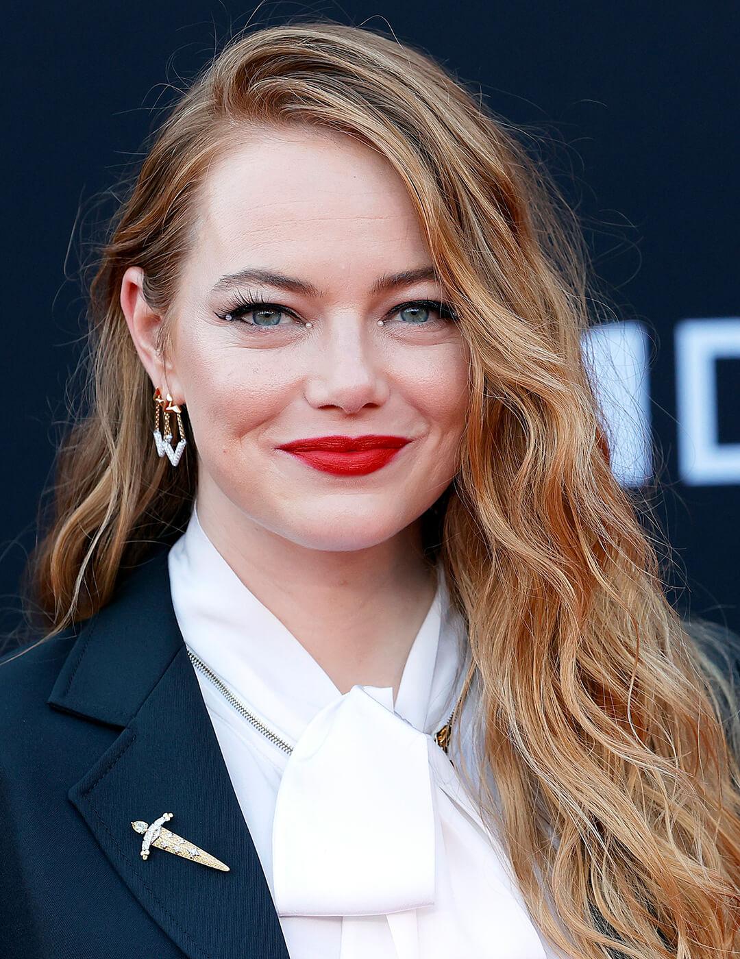 A photo of Emma Stone with strawberry golden hair with pearl beads on her eyelids and wearing a bold red lipstick